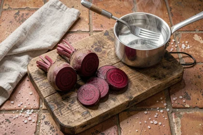 Betteraves rouges entières et tranchées sur une planche en bois rustique, avec une casserole pour la cuisson, idéal pour le borscht